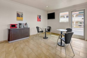 A hotel room with a kitchenette, two chairs, a small table, a flat-screen TV, and a window with a view of the street. - 1 King Bed | Non-Smoking (Clovis NM)