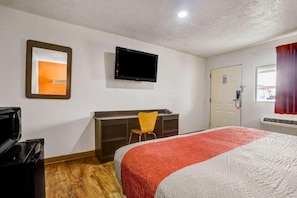 A hotel room with a bed, a desk, a chair, a television, and a door. - 1 King Bed | Non-Smoking (Clovis NM)