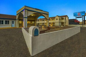 A motel with a central building, a covered parking area, and a sign indicating the number 6. - 1 King Bed | Non-Smoking (Clovis NM)
