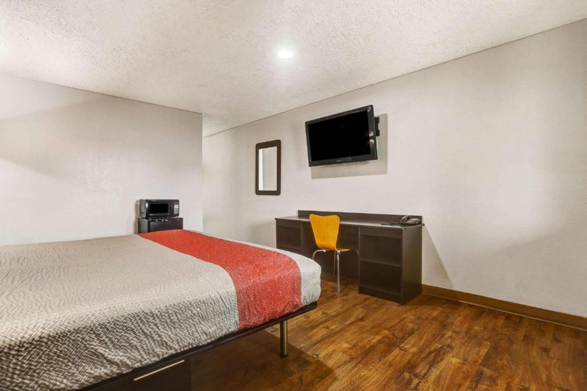 Ein kleines Zimmer mit einem Einzelbett, Holzboden, Schreibtisch mit Stuhl, flachbildschirmfernseher an der Wand und einer Minianlage.