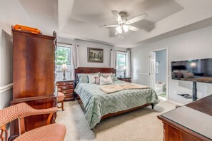 Une chambre à coucher avec un lit, une commode en bois, un téléviseur et un ventilateur de plafond.