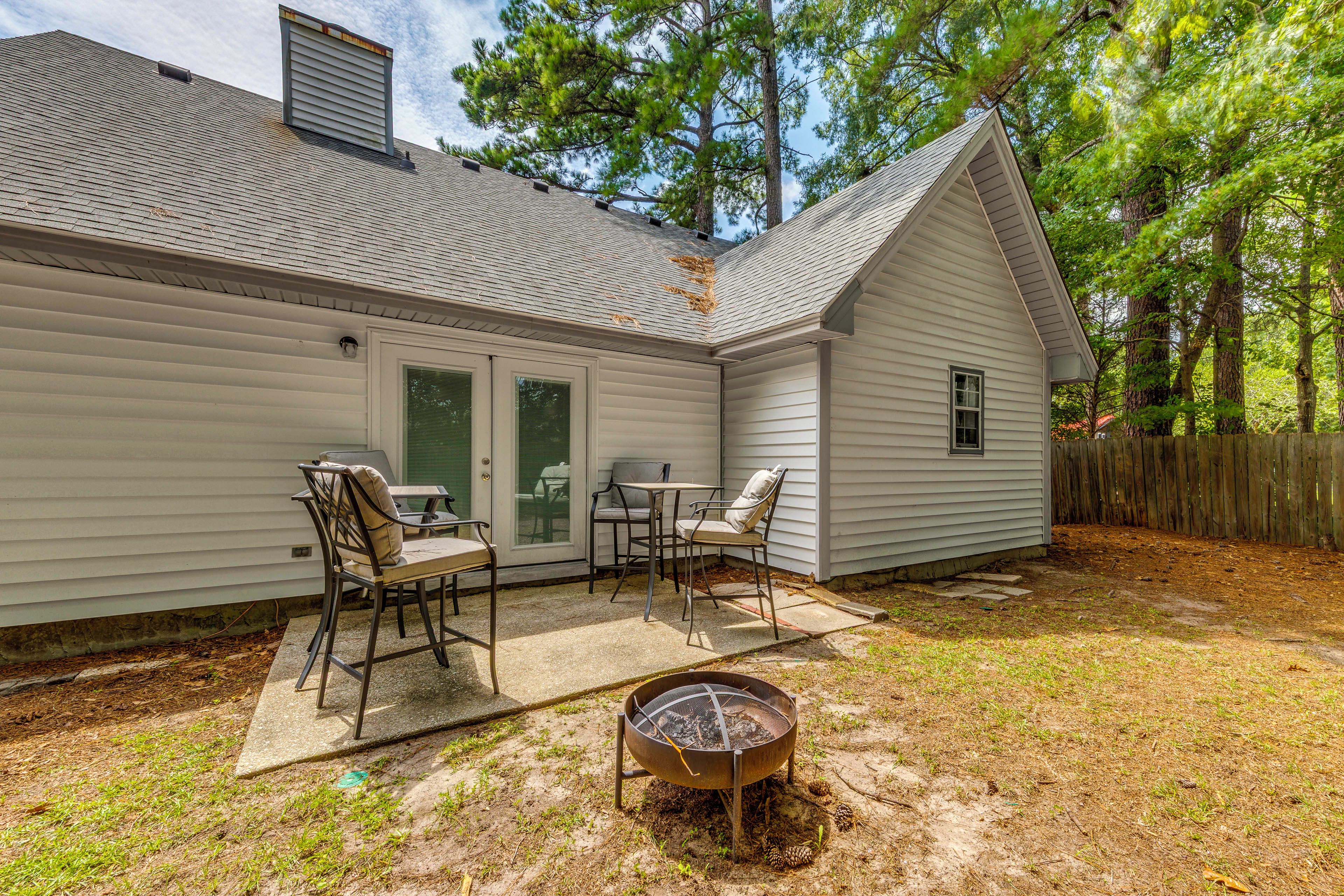 A residential backyard with a covered patio area, a fire pit, and a wooden fence.