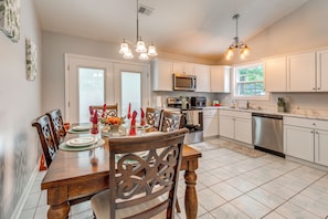 A modern kitchen with white cabinets, stainless steel appliances, and a dining area with a wooden table set for four. - Pet-Friendly Private Yard Near Charleston, Beaches (Goose Creek)