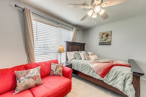 A bedroom with a bed, a red sofa, a ceiling fan, and a window with blinds. - Pet-Friendly Private Yard Near Charleston, Beaches (Goose Creek)