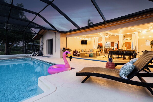 A swimming pool with a flamingo float, lounge chairs, and a covered outdoor area with string lights.