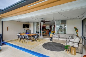 Un espacio exterior cubierto con mesa, sillas, sofá y ventilador de techo.