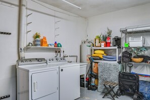 A laundry room with a washer and dryer, shelves with cleaning supplies, a vacuum cleaner, and a cart with bags.