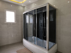 Ein modernes Badezimmer mit einer Glaskabine für die Dusche, einem Fenster mit Jalousien und einem hellen Boden.