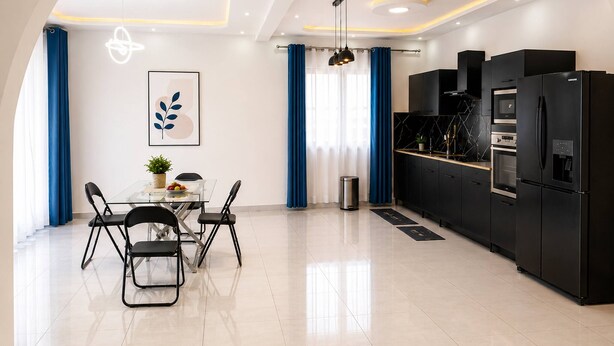 A modern kitchen with black appliances, a dining area with a glass table, and blue curtains. - Modern Apartment • Free WiFi & Airport Transfer (Antananarivo)
