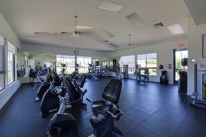 A gym with various exercise equipment, large windows, and an exit sign.