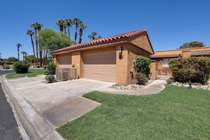 A residential property with a garage, a well-maintained lawn, and tall palm trees in the background. - Sunrise Country Club Condo w/ Pool & Tennis (Rancho Mirage)