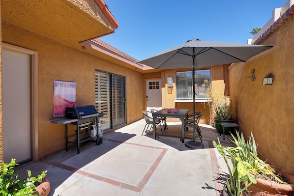 A patio area with a grill, table, chairs, and a large umbrella.