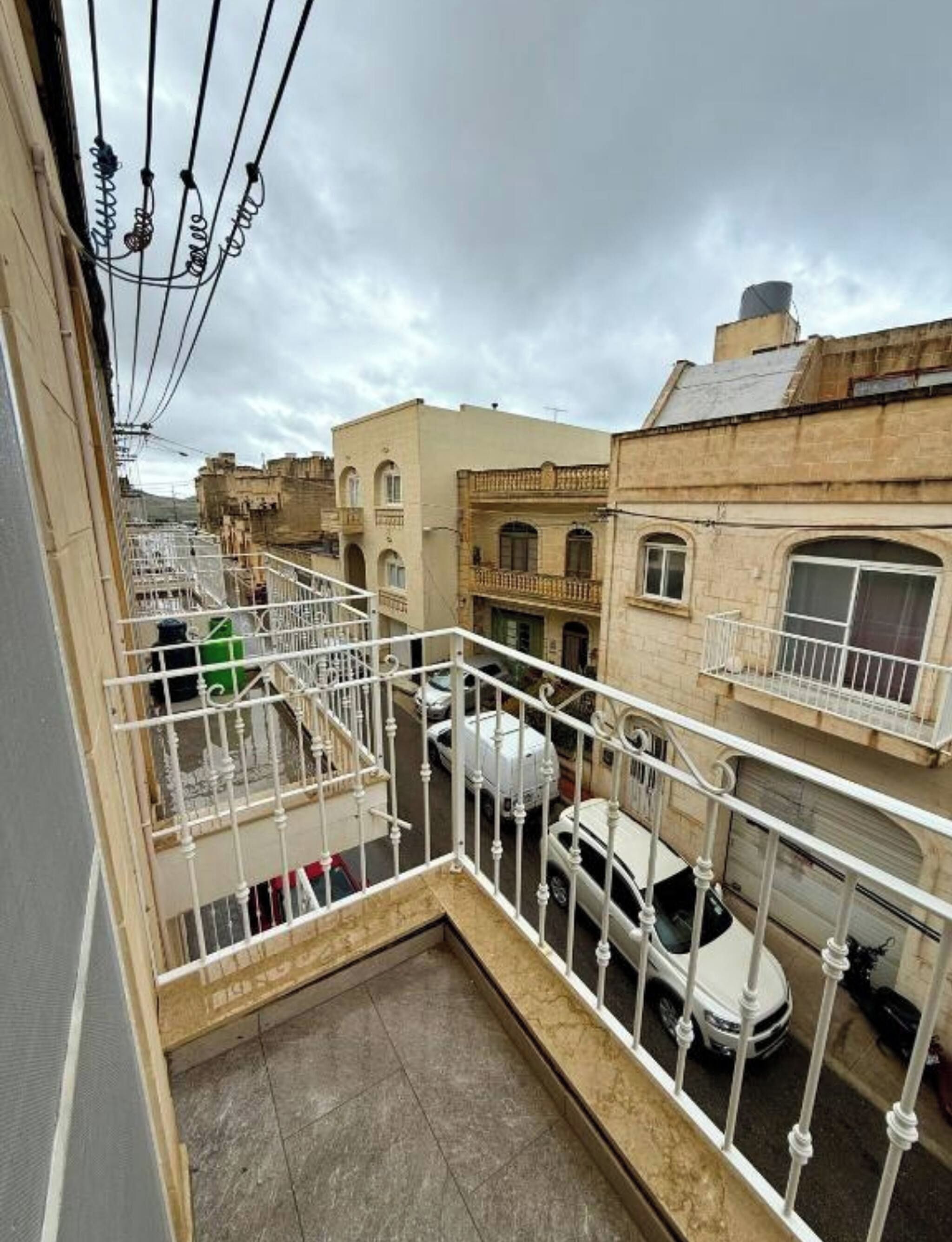 A residential area with a balcony overlooking a street with parked cars and neighboring buildings.