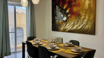 A dining area with a table set for four, a large abstract painting on the wall, and a view through the glass door.