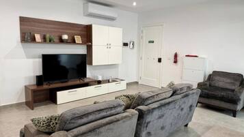 A modern living room with a flat-screen TV, a sofa, a cabinet, and a door marked 'EXIT'.