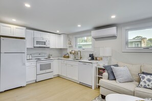 A modern kitchen with white cabinetry, a built-in microwave, a stove, and a dishwasher. There is a window above the sink, and a white sofa with cushions in the adjacent living area. - Sun, Surf & Seafood: York Home 2 Blocks to Beach (York)