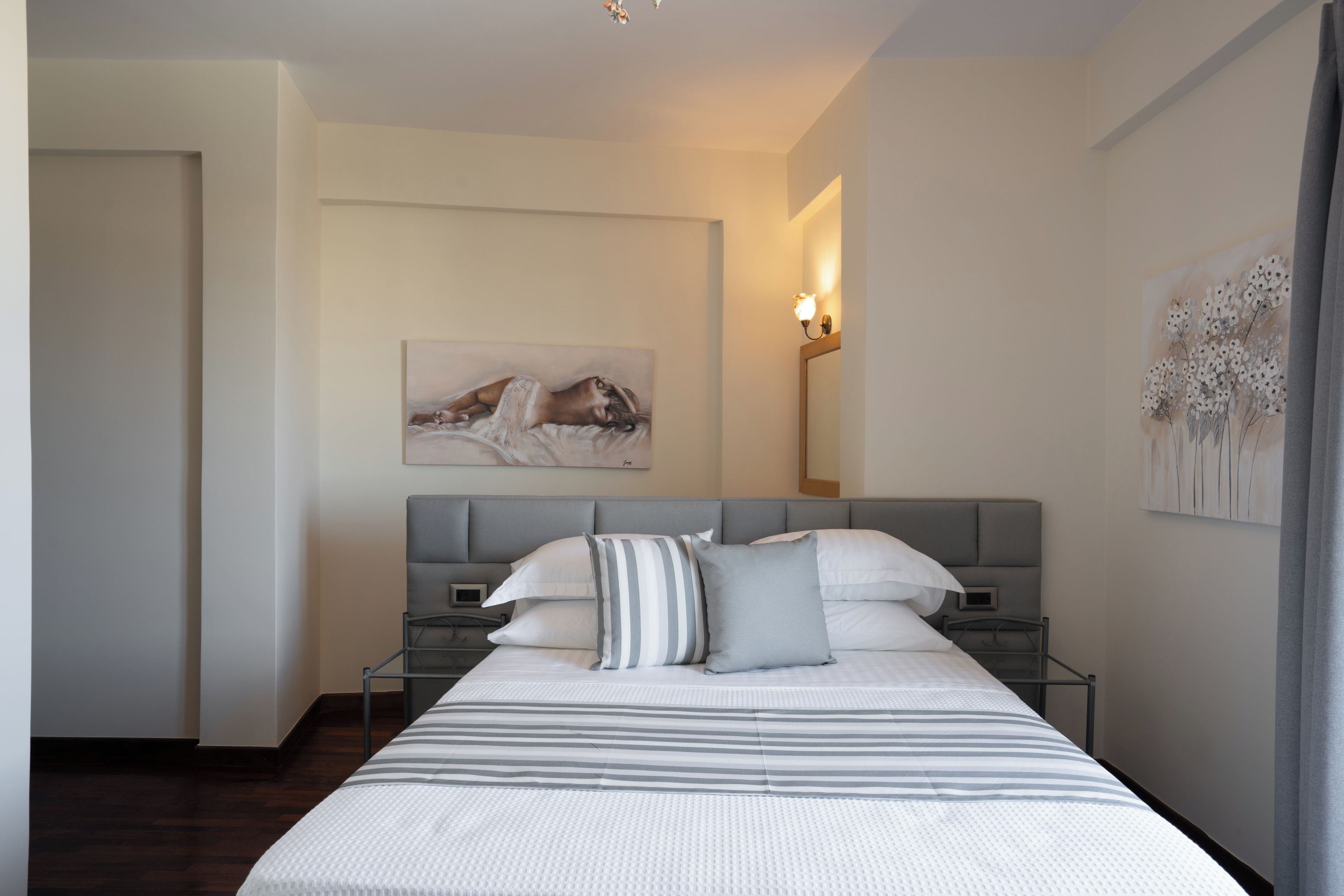 A modern bedroom with a large bed, a headboard, bedside tables, and a painting on the wall.
