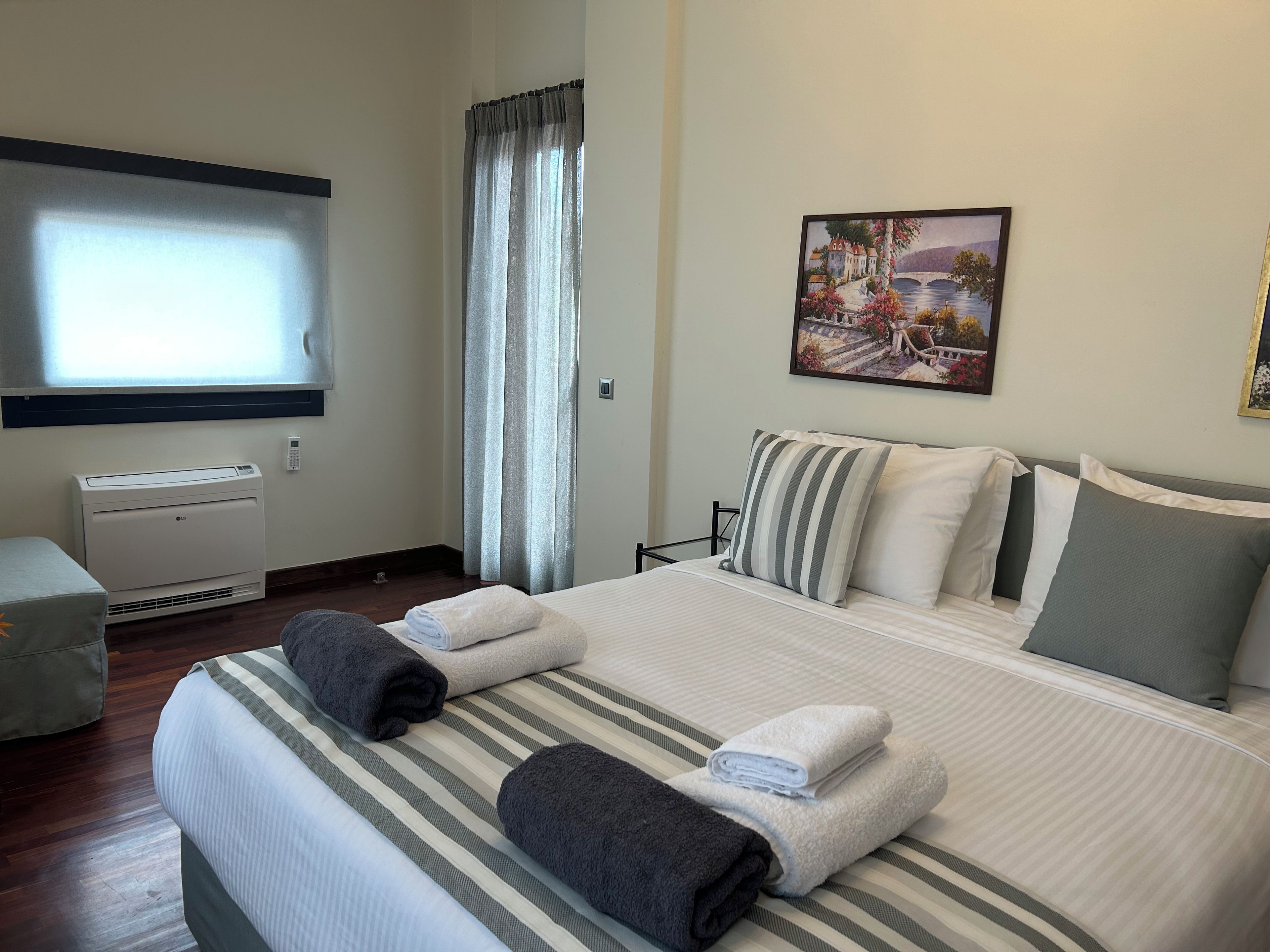 Quarto de hotel com cama, janela com cortinas, ar condicionado e um quadro na parede.