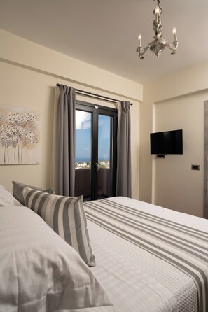 Un dormitorio con una cama, un televisor en la pared y vista al mar a través de una puerta corrediza.