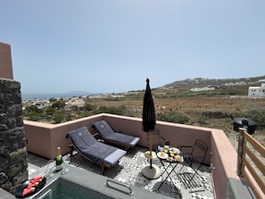 Una terraza en la azotea con sillones, una mesa con desayuno y vistas del paisaje.