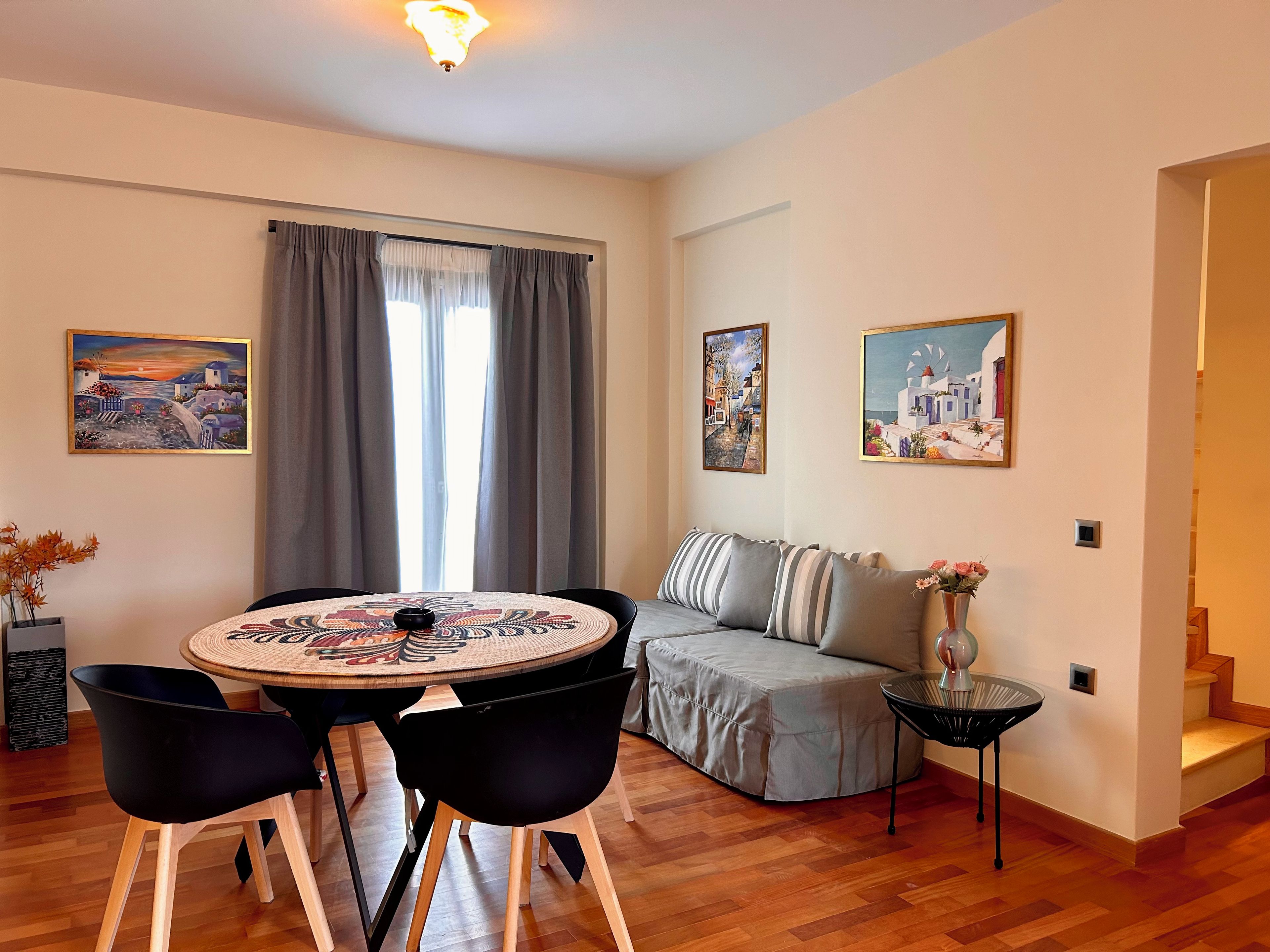 A living room with a round table, black chairs, a grey sofa, and two paintings on the wall.