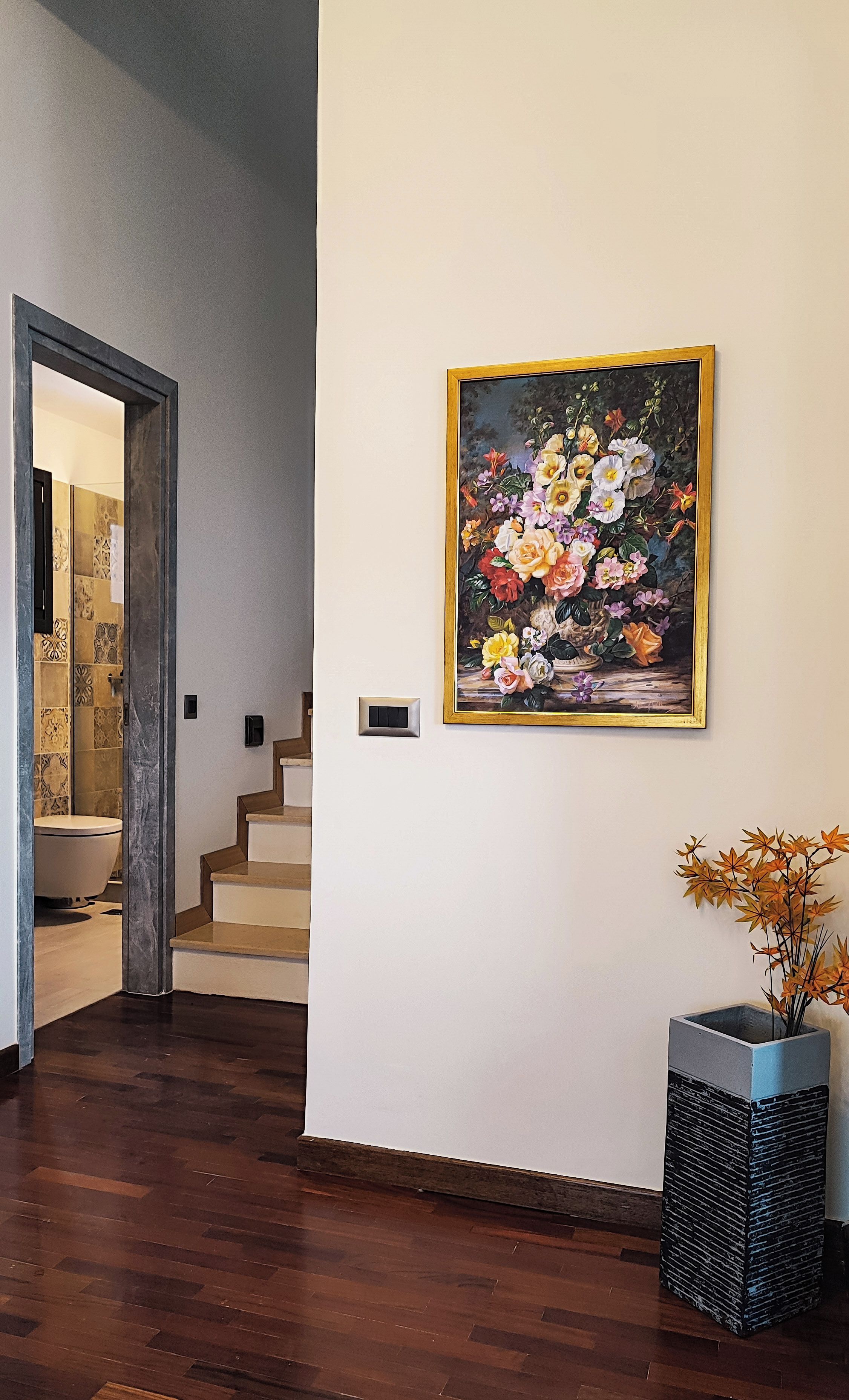 A staircase leading to a bathroom with a tiled wall and a framed floral painting on the adjacent wall.