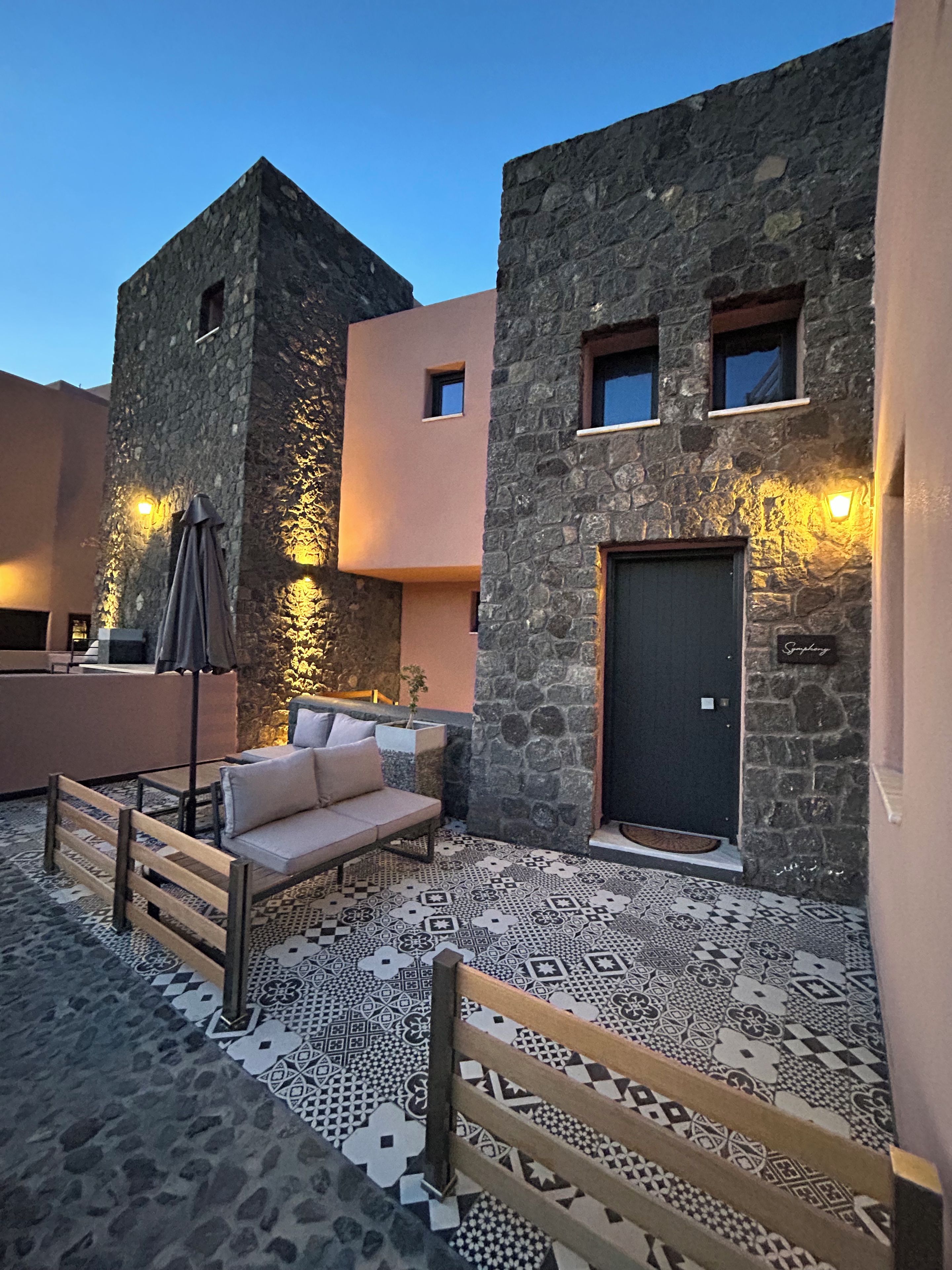 A courtyard with a stone wall, a sofa, a bench, and a door.