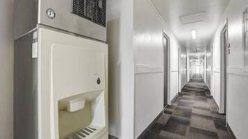 A hotel hallway with a refrigerator on the left, doors on both sides, and a checkered carpet.