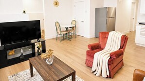Ein modernes Wohnzimmer mit einem Flachbildfernseher, einem Holztisch, einem roten Sessel und einem Essbereich mit Tisch und Stühlen.