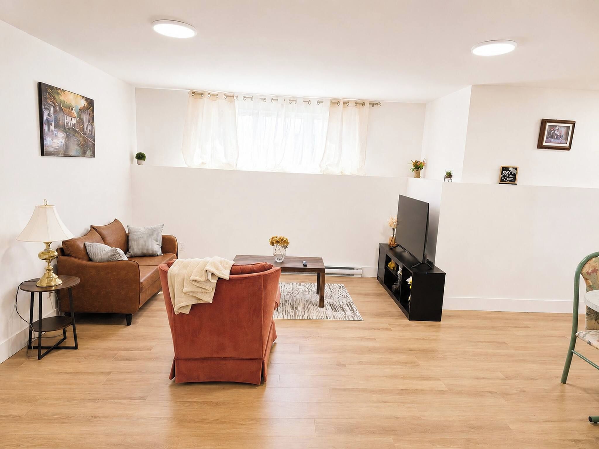 Una sala de estar con un sofá marrón, un sillón rojo, una mesa de centro, un mueble para televisión y una lámpara.