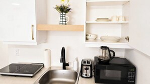 Eine Küche mit Spüle, Toaster, Kaffeemaschine und einem weißen Schrank mit oberem Regal.