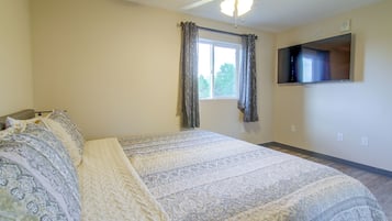 Ein Schlafzimmer mit einem Bett, einem Deckenventilator, einem Fenster mit Vorhängen, einem an der Wand befestigten Flachbildfernseher und einer Steckdose.