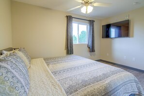 Ein Schlafzimmer mit einem Bett, einem Deckenventilator, einem Fenster mit Vorhängen, einem an der Wand befestigten Flachbildfernseher und einer Steckdose.