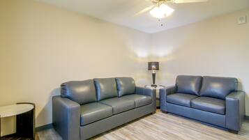 A room with two grey leather sofas, a small table with a lamp, and a ceiling fan.