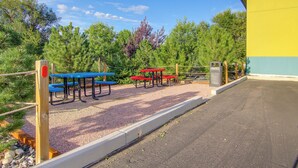 Un'area salotto all'aperto con tavoli da picnic e panchine, circondata da alberi e un edificio.