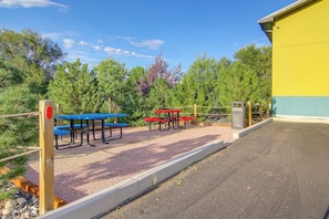 An outdoor seating area with picnic tables and benches, surrounded by trees and a building. - See the Royal Gorge! Cañon City Apartment (Cañon City)