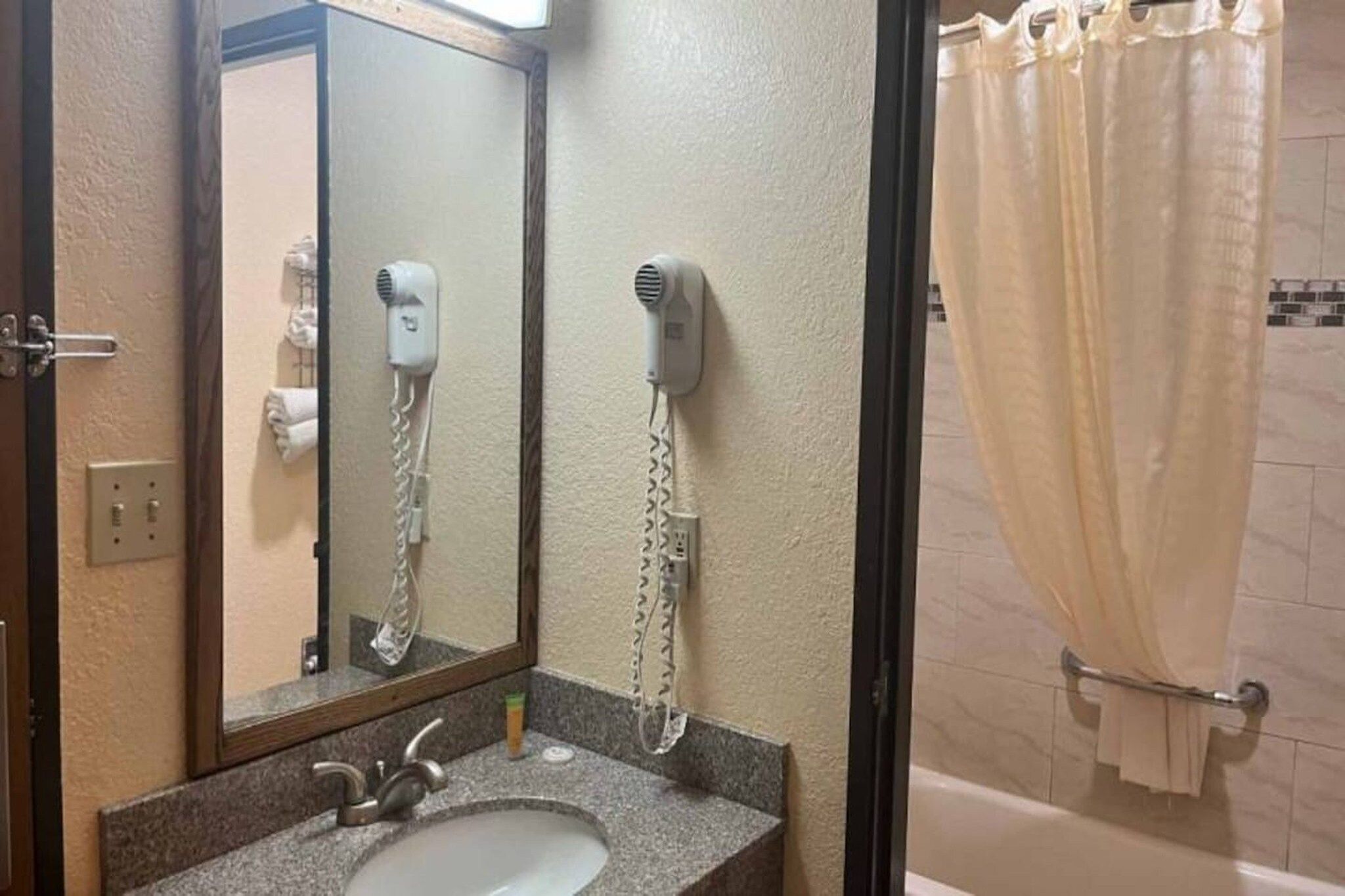 A bathroom with a sink, mirror, hair dryer, and shower curtain.