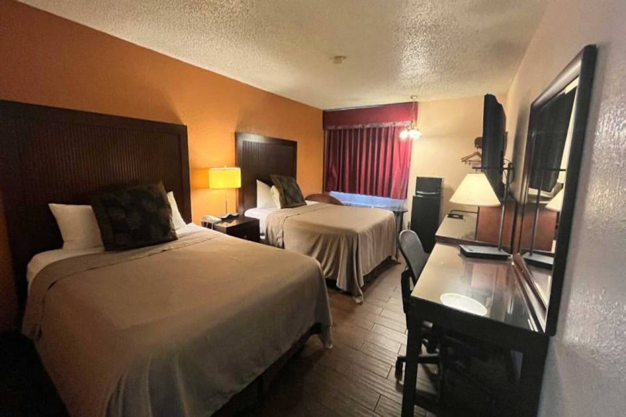 Une chambre d’hôtel avec deux lits, un bureau, une chaise, une télévision et une fenêtre avec des rideaux.