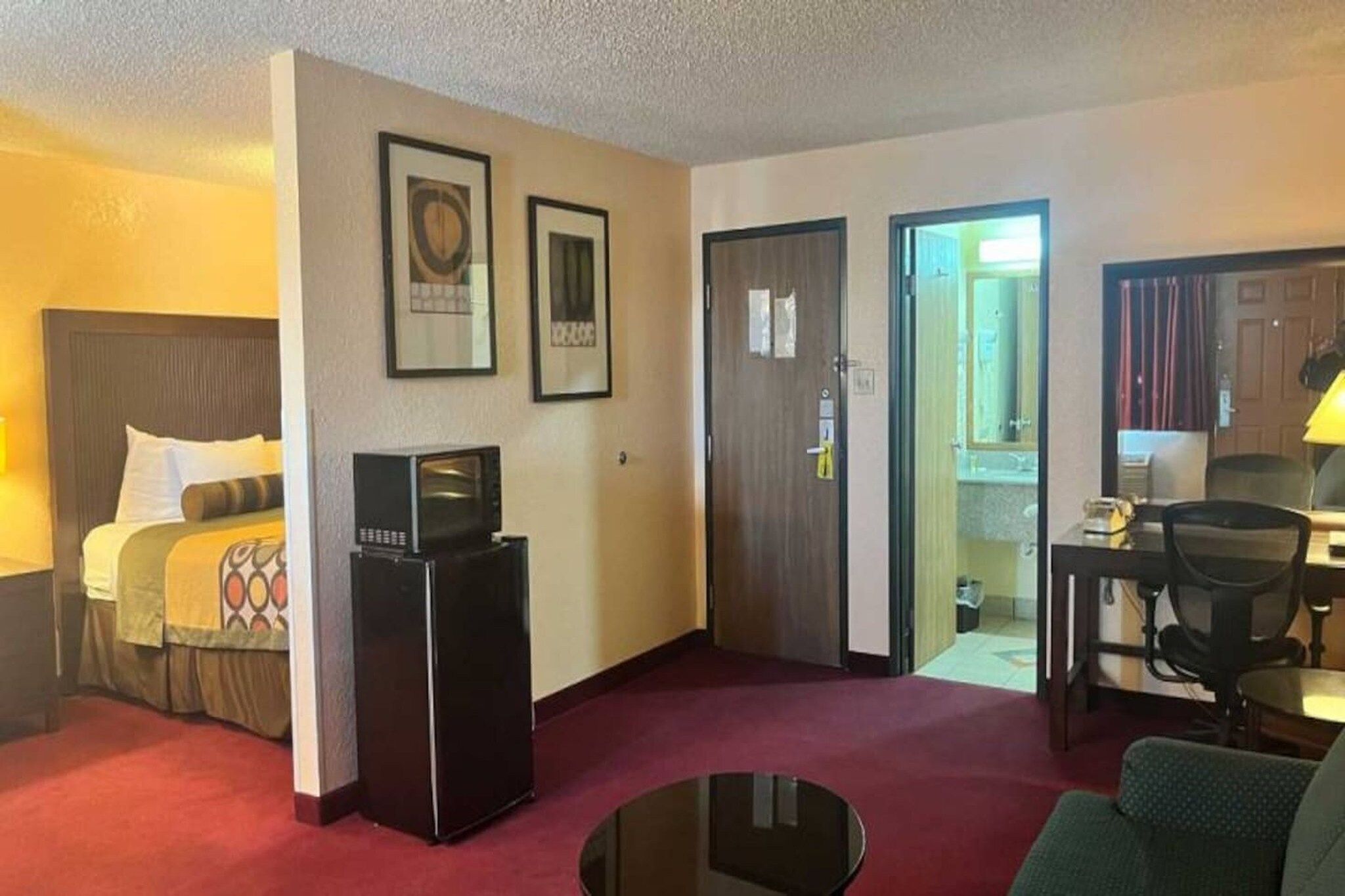 Hotellihuone, jossa on sänky, jääkaappi, työpöytä, tuoli ja ruokailutila.