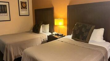 Habitación de hotel con dos camas individuales, una mesita de noche con lámpara y cuadros en la pared.