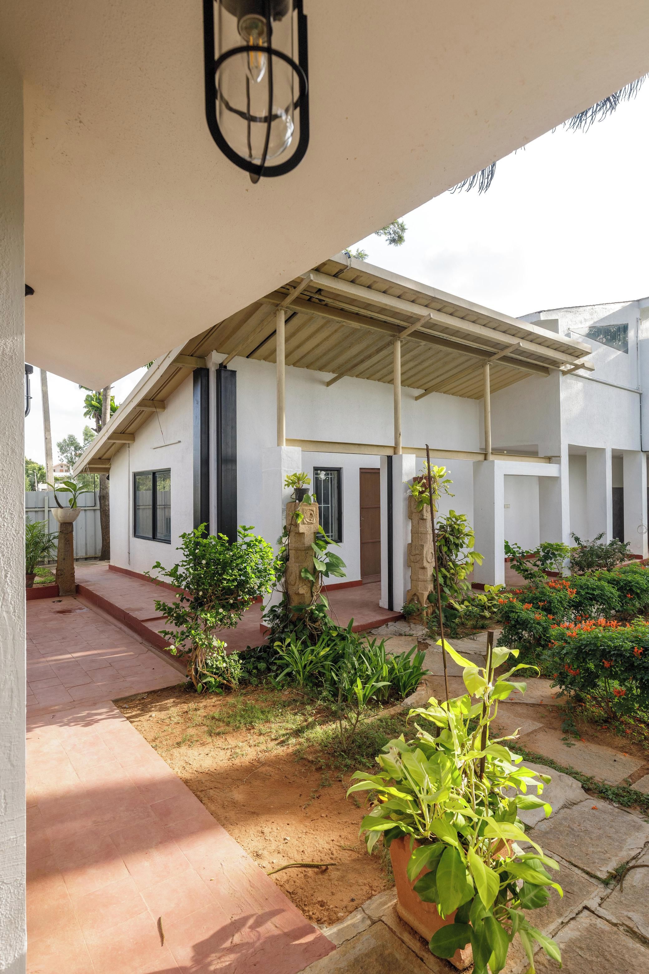 A covered outdoor area with a pathway leading to a building, surrounded by potted plants and a small garden.