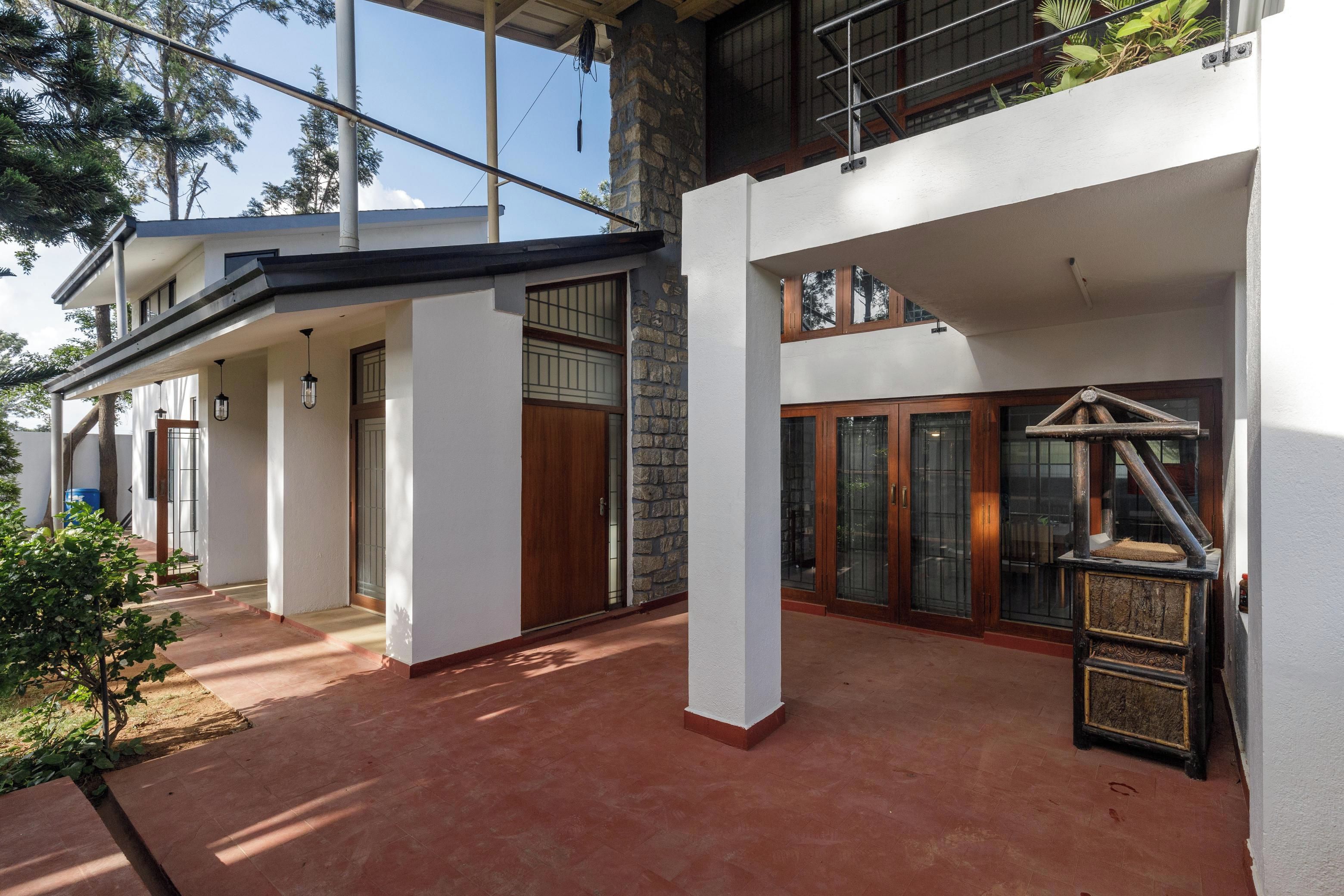 A modern two-story house with a covered patio area, large windows, and a stone wall.