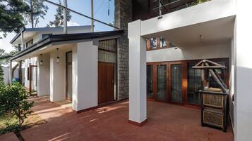 A modern two-story house with a covered patio area, large windows, and a stone wall.