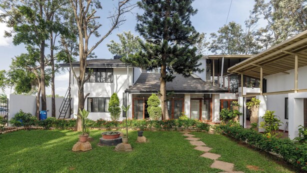 Una moderna casa a due piani con un giardino curato, un vialetto in pietra e diversi alberi.