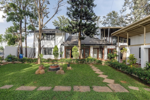 A modern two-story house with a well-maintained garden, stone pathway, and a variety of trees. - Grandeur 5bhk Villatheatre Hennurmanyata (Bengaluru)