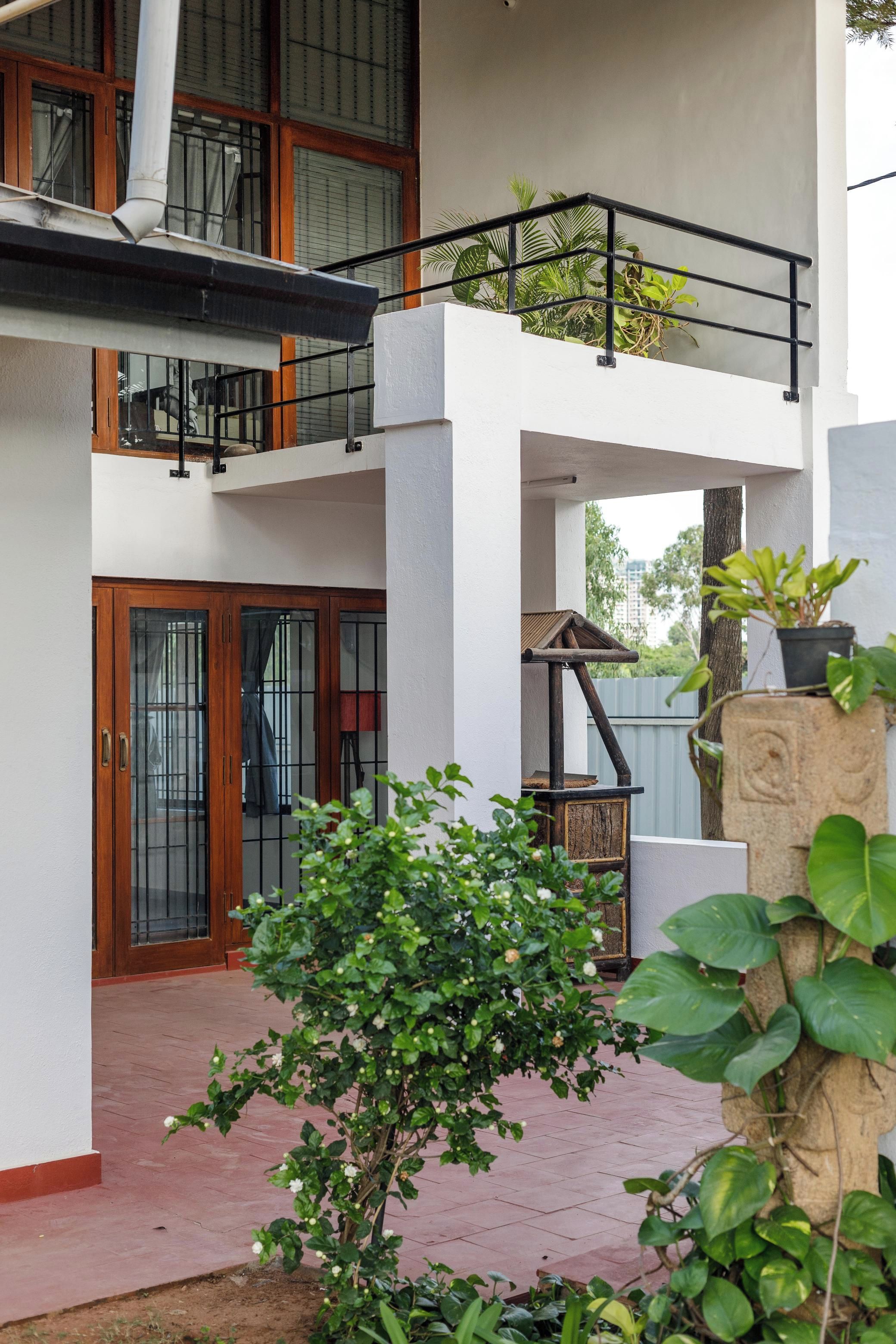 A two-story building with a balcony, a wooden door, and a small garden area.