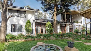 Una moderna casa a due piani con un giardino curato, che include uno stagno con ninfee.
