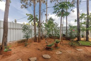 A garden with tall trees, potted plants, and a dirt ground. - Grandeur 5bhk Villatheatre Hennurmanyata (Bengaluru)