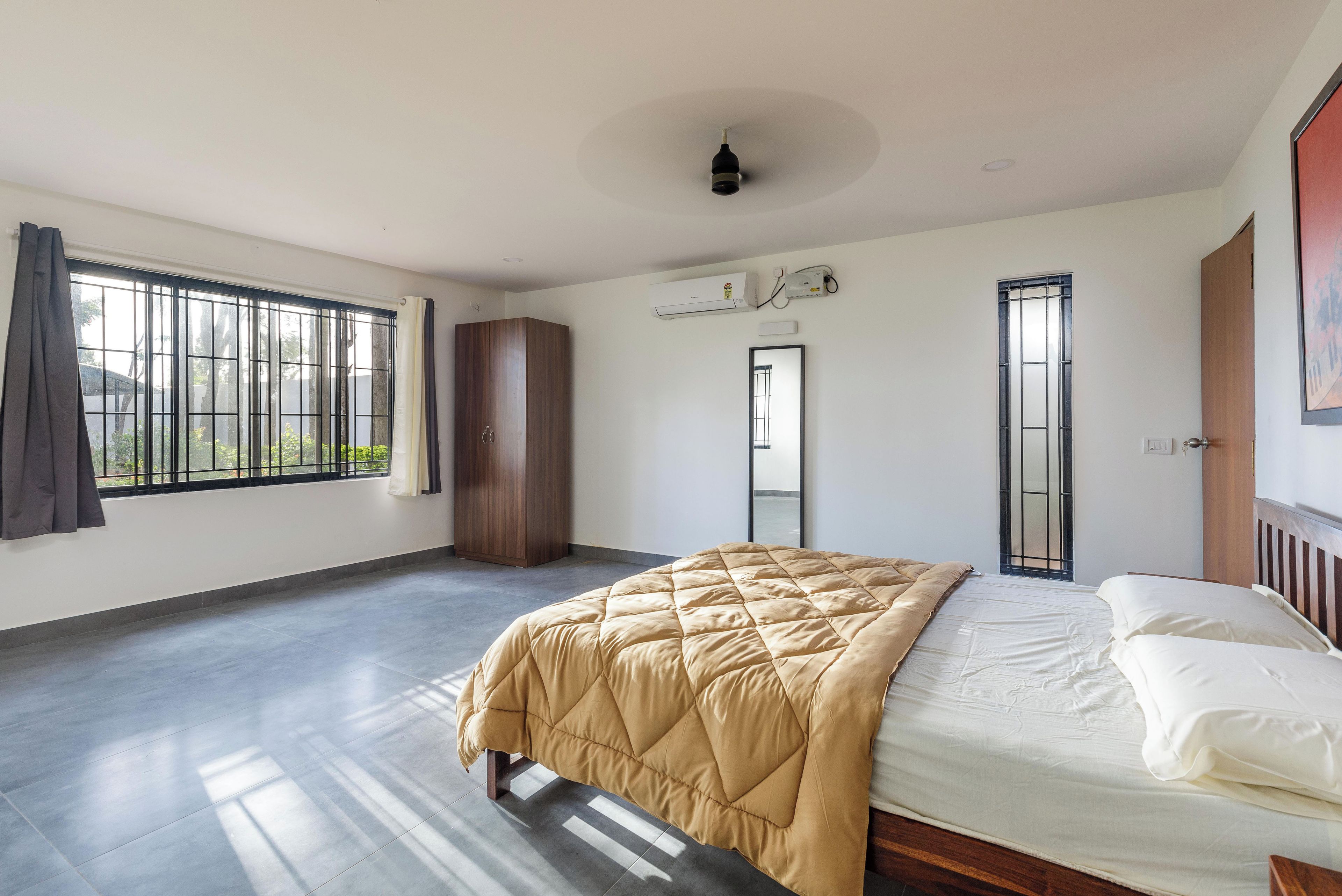 A bedroom with a bed, a wardrobe, a window with a view, and an air conditioning unit.