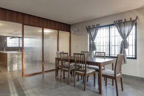Uma área de refeições com mesa e cadeiras de madeira, porta deslizante e janela com cortinas.